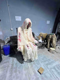 Seated animatronic zombie in white robe seen from behind